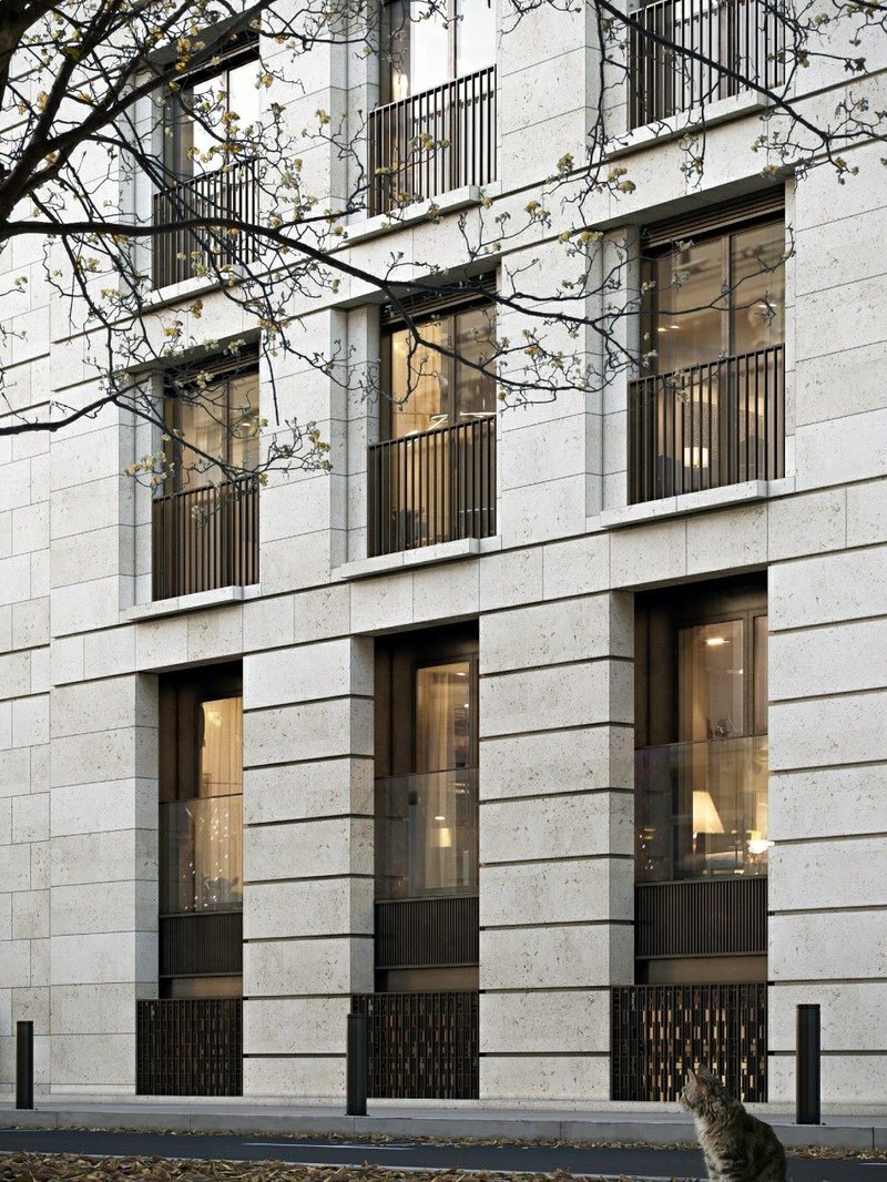 Pale-stone London apartment building with black balconies behind a tree