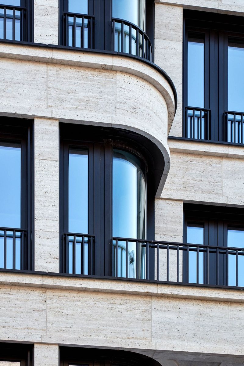 Curved travertine facade with tall windows and black iron balconies